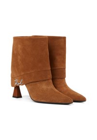 Stivaletti in suede marrone con risvolto, punte appuntite e un tacco a blocco corto. Il dettaglio in argento sul risvolto aggiunge un accento distintivo.