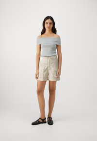 Svetlošedý rebrovaný top s odkrývajúcimi ramenami skombinovaný s béžovými šortkami so cargo vreckami a pásom na sťahovanie. Čierne sandále dotvárajú outfit.