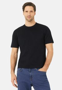 Černé tričko s krátkým rukávem z bavlny, s klasickým kulatým výstřihem a standardním střihem. Nosené s modrými džíny, vytváří uvolněný vzhled.
