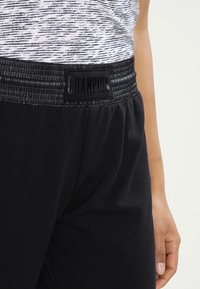 Black sweatpants with a textured elastic waistband featuring a black "CHAMPION" logo. Soft, lightweight material with a relaxed fit.