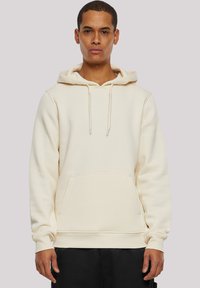 Hoodie crème avec une poche avant, capuche à cordon, poignets côtelés et texture douce. Design simple, adapté aux vêtements décontractés.