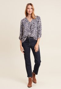 Hemd mit blau-weißem Muster und V-Ausschnitt, 3/4-Ärmeln, kombiniert mit dunkelblauen Jeans und braunen Stiefeletten.