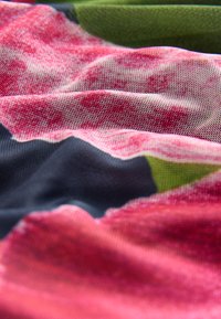 Textil mit einer Mischung aus rosa, grün und dunkelblauen Mustern, mit einer weichen, strukturierten Oberfläche und sichtbaren Mesh-Details im Stoff.
