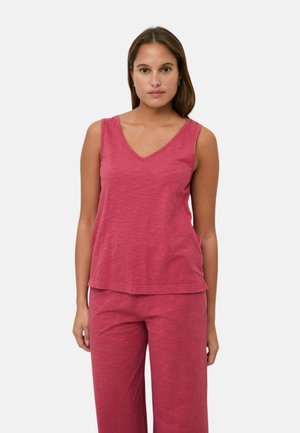 Mujer con camiseta sin mangas de escote en V rosa y pantalones anchos a juego, de pie frente a un fondo claro y liso.