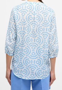 Blusa trasparente con motivo a spirale blu tie-dye, caratterizzata da maniche a tre quarti e un orlo arrotondato. Tessuto leggero e texturizzato.