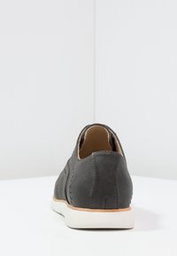 Chaussure en cuir gris avec une texture lisse, bout rond et semelle en caoutchouc blanc. Présente des détails de couture et un design à dos ouvert.