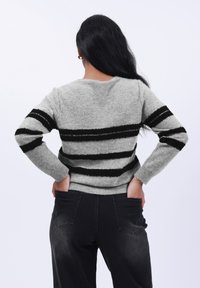 Grauer gestreifter Pullover mit schwarzen strukturierten Streifen, runder Ausschnitt, gerippte Bündchen und Saum, kombiniert mit hoch taillierten schwarzen Jeans.