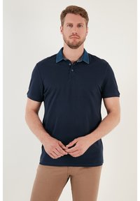Námořnická modrá polo tričko s límcem připomínajícím denim, krátkými rukávy a propracovaným střihem. Přední část obsahuje tříknoflíkovou légu a jemné švy.