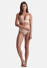 Nude dwuczęściowy komplet bielizny składający się z biustonosza z głębokim dekoltem i regulowanymi ramiączkami oraz wysokich, bezszwowych majtek typu bikini w elastycznym materiale.