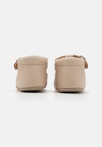 Beige skinnysko uten snøring med en glatt overflate, myk rund tå og en dekorativ vevd aksent nær hælen.