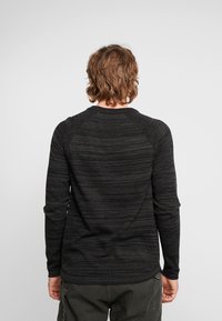 Chemise noire à manches longues avec un motif rayé texturé et des manches raglan. Tissu lisse et ourlet inférieur arrondi. Coupe décontractée.