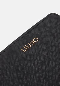 Portafoglio nero con texture realizzato in materiale sintetico, con logo "LIU·JO" in oro goffrato. Presenta un bordo liscio e dettagli raffinati.