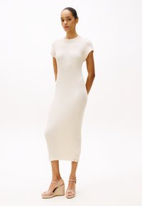 Ribbed knit dress in off-white, mid-length with short sleeves. Paired with beige wedge sandals featuring ankle straps and woven detailing.