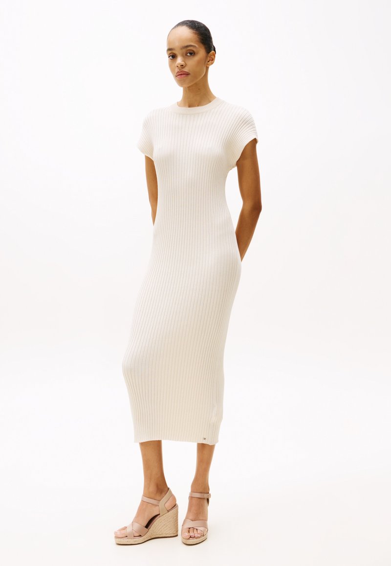 Ribbed knit dress in off-white, mid-length with short sleeves. Paired with beige wedge sandals featuring ankle straps and woven detailing.