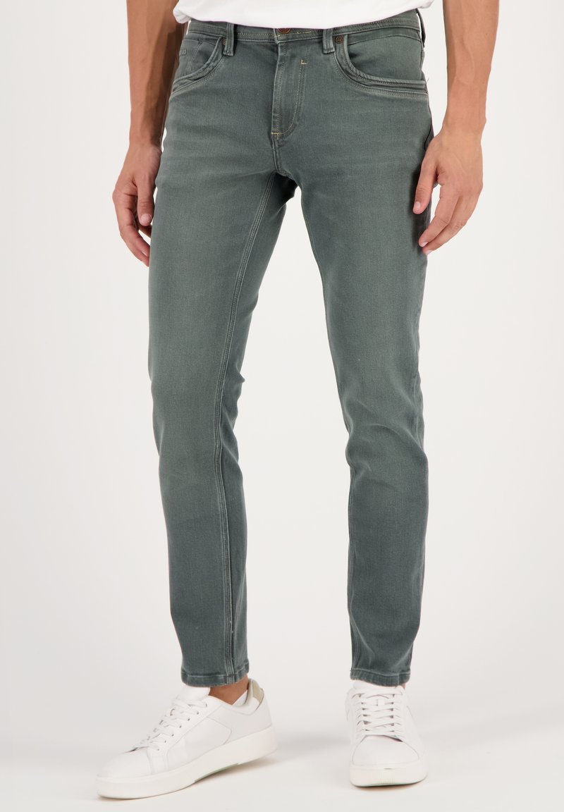 Vihreät farkut, joiden slim fit -leikkaus on klassinen viiden taskun muotoilu, hienovarainen ompelu ja valkoiset tennarit.