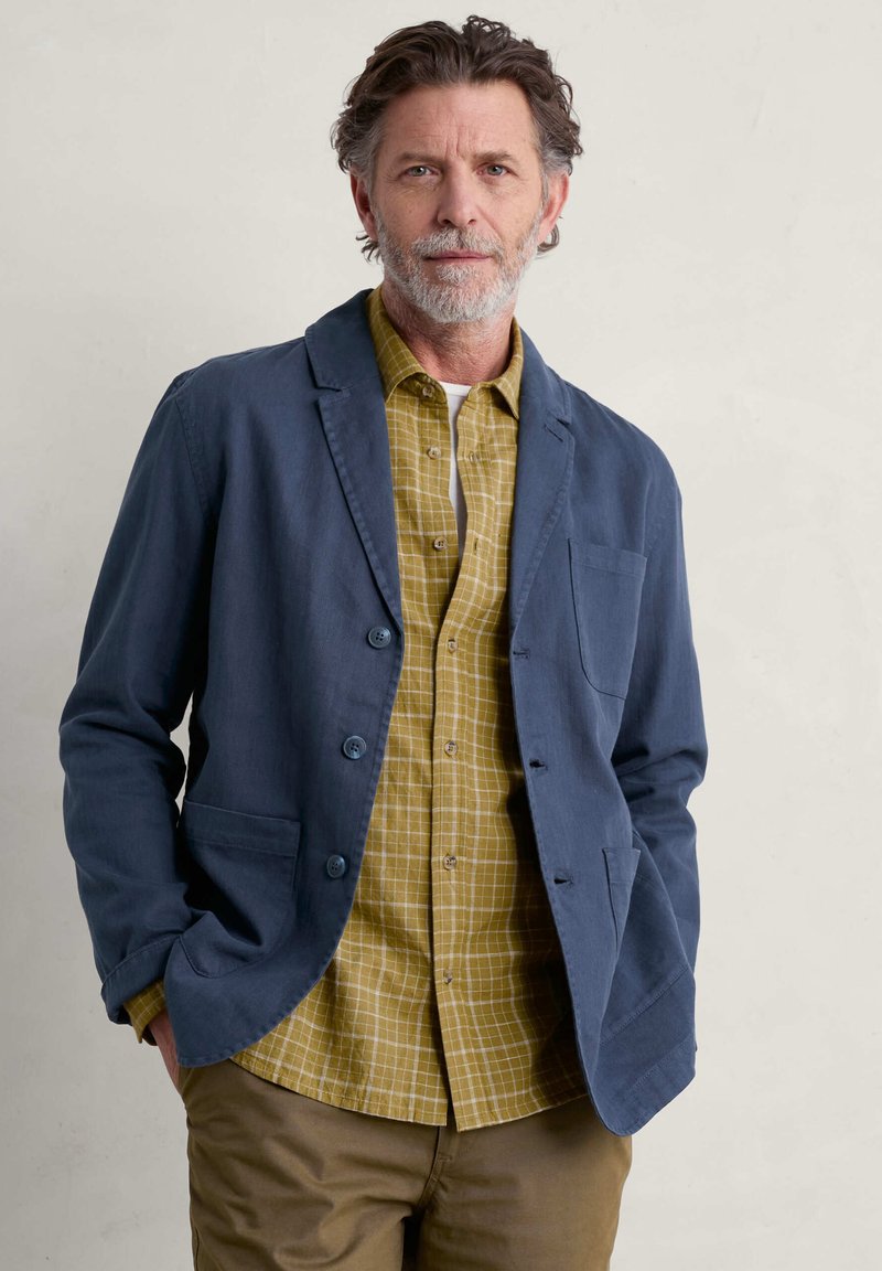 Marineblauer Blazer mit weicher Textur, einer Brusttasche und zwei vorderen Taschen, kombiniert mit einem gelben Karoshirt. Lässiger, entspannter Schnitt.