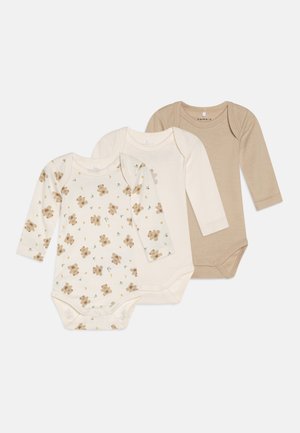 Três bodysuits de manga longa: um em creme com estampa de ursinho de pelúcia, um em creme liso e um em bege claro. Feitos de um suave tecido de algodão.