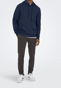Felpa con cappuccio blu navy con tasca frontale, abbinata a pantaloni a scacchi grigi e sneaker bianche. Tessuto morbido con una vestibilità rilassata.