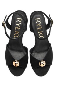 Czarne zamszowe sandały z krzyżowymi paskami, otwartym noskiem i złotym akcentem w postaci guzika. Regulowany pasek wokół kostki zapewniający bezpieczne dopasowanie.