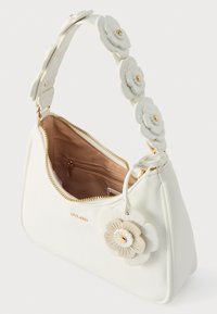 Sac à main blanc avec une surface texturée, un accent floral sur la lanière, une quincaillerie dorée et une fermeture éclair. L'intérieur présente une doublure beige.