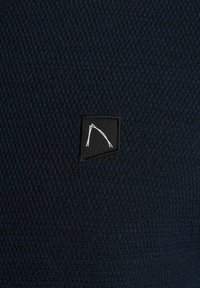 Marineblaue strukturierte Stoff mit einem engmaschigen Muster. Verfügt über ein schwarzes quadratisches Etikett mit einem weißen Liniendesign. Eignet sich für Freizeitkleidung.