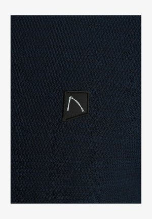 Tejido texturizado en color marino con un patrón de tejido cerrado. Presenta una etiqueta cuadrada negra con un diseño de línea blanca. Adecuado para el uso casual.