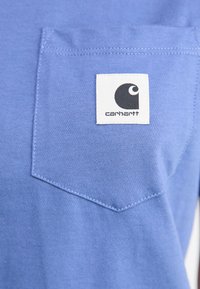 Modra bombažna majica s prsno žepom in črno-belim oznako Carhartt. Gladka tekstura in okrogli izrez.