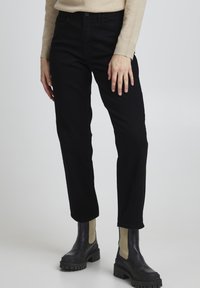Schwarze Denim-Jeans mit geradem Bein, die eine weiche Textur und eine mittlere Taille aufweisen, kombiniert mit klobigen schwarzen Knöchelstiefeln.