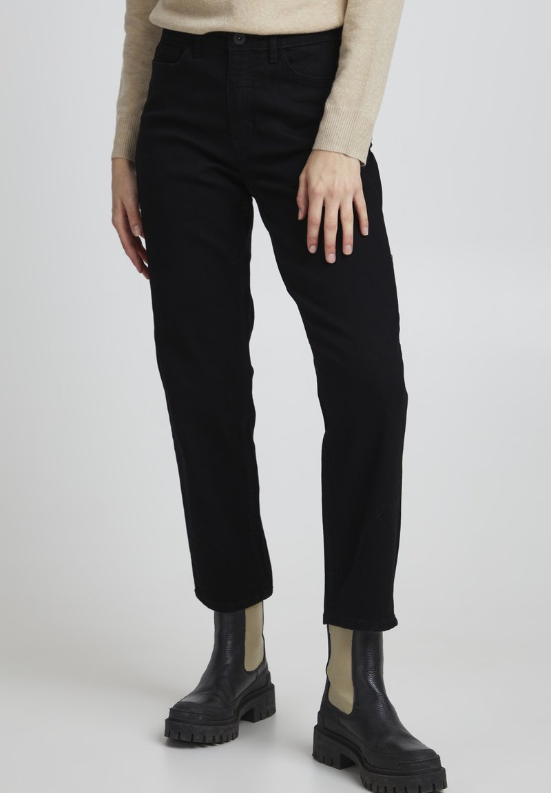Schwarze Denim-Jeans mit geradem Bein, die eine weiche Textur und eine mittlere Taille aufweisen, kombiniert mit klobigen schwarzen Knöchelstiefeln.
