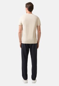 Beige kortærmet t-shirt lavet af blødt stof, parret med marineblå bukser og hvide sneakers, set bagfra.