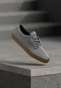 Ανοιχτό γκρι καμβάς αθλητικά παπούτσια με καμηλό ελαστική σόλα, στρογγυλή μύτη και κορδόνια μπροστά. Διαθέτει διακριτική σήμανση και ομαλή υφή.