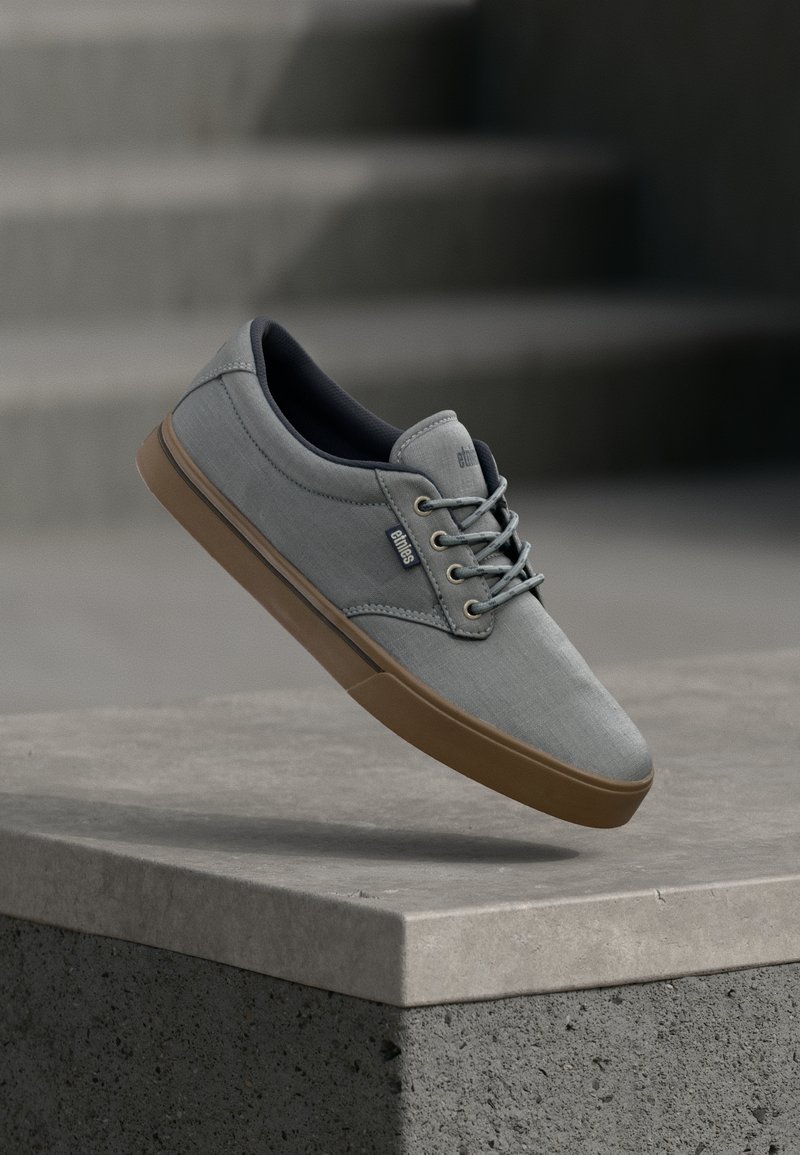 Baskets en toile gris clair avec une semelle en caoutchouc beige, bout rond et lacets à l'avant. Présente une marque discrète et une texture lisse.