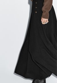 Gonna maxi nera con una silhouette fluida. Presenta dettagli con bottoni sul davanti, abbinata a un maglione in maglia marrone con texture.