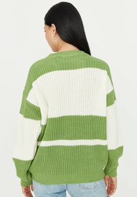 Donna con long hair scuro che indossa orecchini a cerchio dorati e un maglione lavorato a maglia a righe verde e bianco, girata di spalle rispetto alla macchina fotografica.