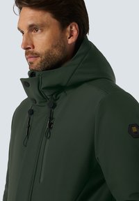 Groene waterdichte jas met hoge kraag, koordjes en zwarte accenten. Heeft een ritszak en een kenmerkende schouderpatch.
