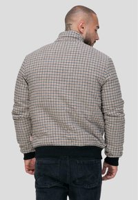 Veste à motif pied-de-poule dans des tons de marron et de crème, avec des poignets et un ourlet côtelés, un col montant, fabriquée à partir d'un tissu texturé.