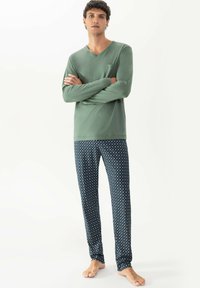 Groene lange mouwen top met een V-hals en een borstzak, gecombineerd met marineblauwe pyjamabroek met een geometrisch patroon.