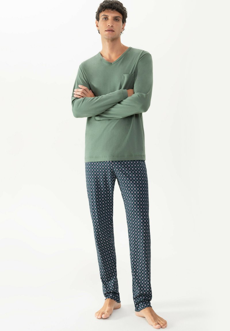 Groene lange mouwen top met een V-hals en een borstzak, gecombineerd met marineblauwe pyjamabroek met een geometrisch patroon.