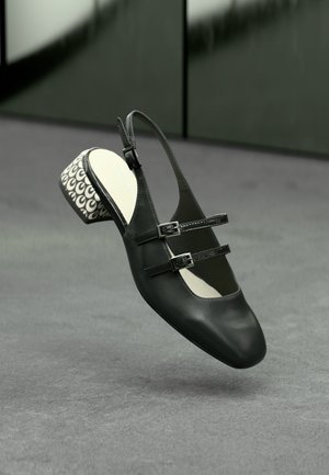 Černé kožené slingback boty s dvojitými popruhy, které mají vzorovanou bílou a černou blokovou podpatek a hladký, zaoblený tvar špičky.