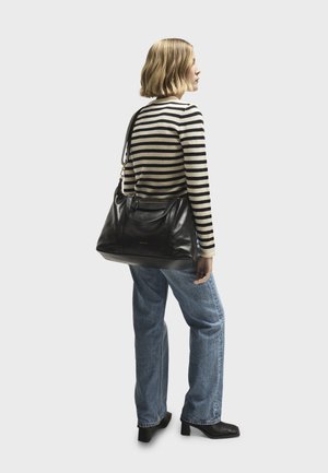 Borsa a tracolla in pelle nera con doppi manici e tracolla, dotata di hardware dorato, abbinata a una maglietta a righe a maniche lunghe e jeans blu.