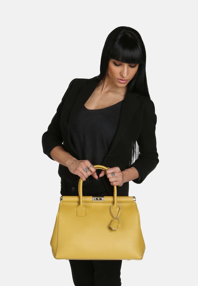 Gul läderhandväska med en strukturerad design, ovandelshandtag och en avtagbar bagagetagg. Slät yta och blanka metallbeslag.