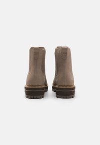 Bottes chelsea en daim marron avec des panneaux latéraux élastiques, semelles marron contrastantes et un détail cousu à la base et au talon.