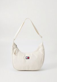 Krémově zbarvená kabelka přes rameno se zipovým uzávěrem a nastavitelným popruhem, s malým obdélníkovým logem Tommy Jeans uprostřed přední strany.