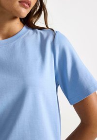 Lichtblauw katoenen T-shirt met ronde hals, korte mouwen en een soepele textuur. Heeft nette naden en een ontspannen pasvorm.