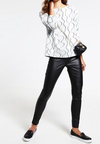 Vitt ribbat linne med svarta vågiga linjer, kombinerat med åtsittande svarta läderleggings och svarta slip-on skor. Liten vävd handväska med kedjesnurra.