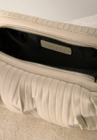 Borsa a tracolla beige in pelle trapuntata con zip argentata parzialmente aperta, che mostra l'interno in tessuto nero e l'etichetta del marchio cucita all'interno.