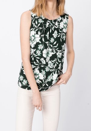 Blouse sans manches à fleurs de couleur vert foncé avec des fleurs blanches et vert clair. Tissu doux, ourlet légèrement courbé, plissage subtil au niveau du col.