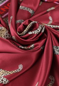 Röd satintextil med leopardmönster i olika nyanser. Tyget är slätt med en glansig yta och faller elegant.