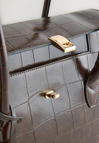 Brown leather handbag with a crocodile pattern, gold hardware clasp, smooth texture, and contrasting stitching detail.
