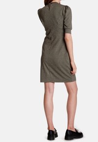 Grön rutigt klänning med korta puffärmar och dragkedja bak. Tyget har en mjuk yta. Bärs med svarta skor.